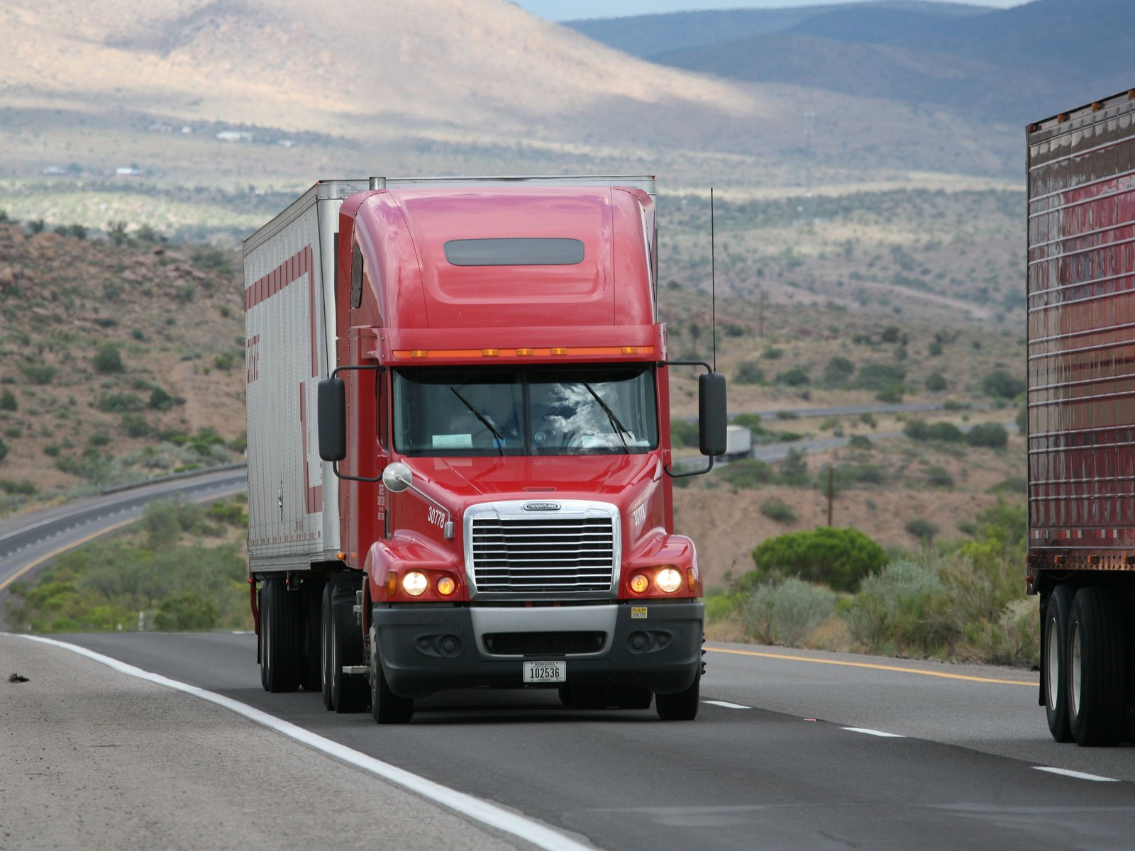 A red semi truck pulling a loaded trailer along an open interstate through high desert country